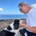Mand kigger på sin hund på strand, mens han sidder ned.