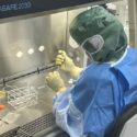 En forsker iført værnemidler sidder i laboratoriet med en pipette.