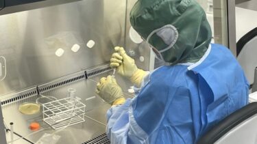 En forsker iført værnemidler sidder i laboratoriet med en pipette.