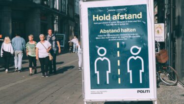 Et skilt i en dansk gåde, der anmoder folk om at holde afstand på grund af corona.