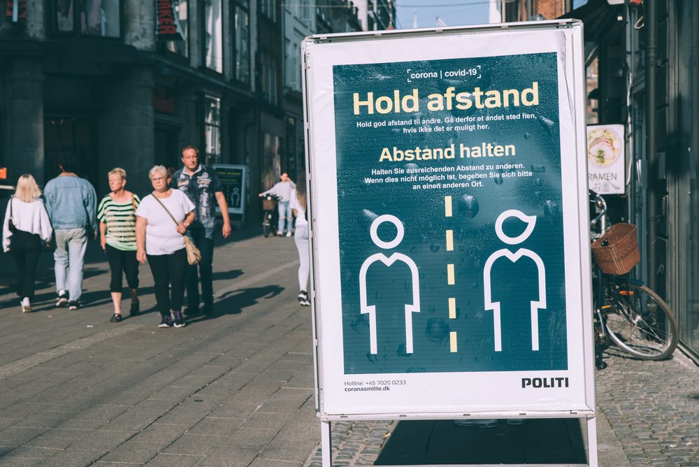 Et skilt i en dansk gåde, der anmoder folk om at holde afstand på grund af corona.