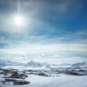 Arktisk landskab med bjerge, sne og sol