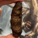 Bromalit, dinolort, holdt af en hånd med et billede af en dinosaur i baggrunden
