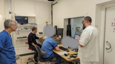 Et computerrum fyldt med forskere og hospitalspersonale. De kigger allesammen i retning af computeren, hvor man kan se fMRI-scanningen