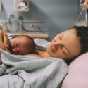 En mor ligger med sit nyfødte barn på en hospitalsseng