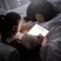 Lille pige sidder i sin seng og læser på en iPad