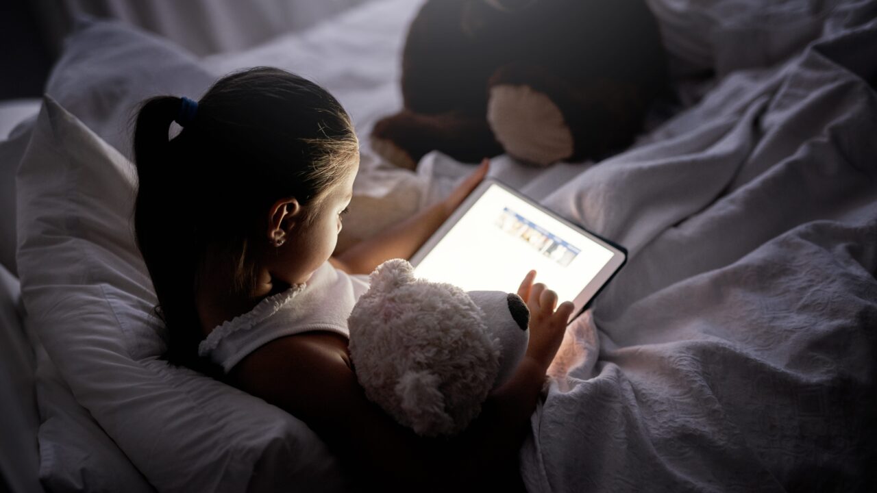 Lille pige sidder i sin seng og læser på en iPad