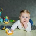 En baby ligger på gulvet og har en hånd i munden