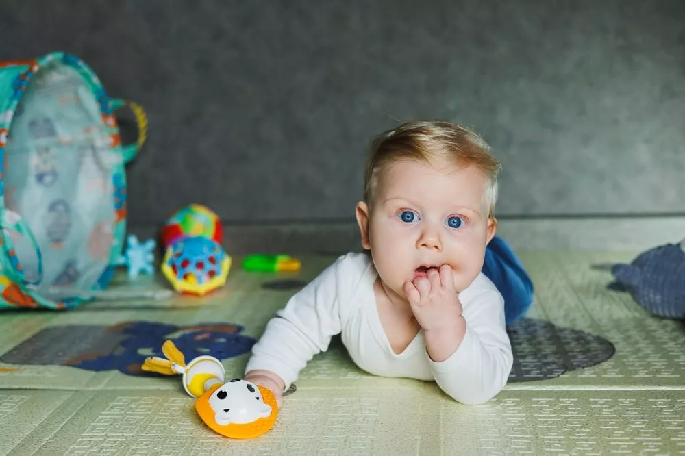 En baby ligger på gulvet og har en hånd i munden