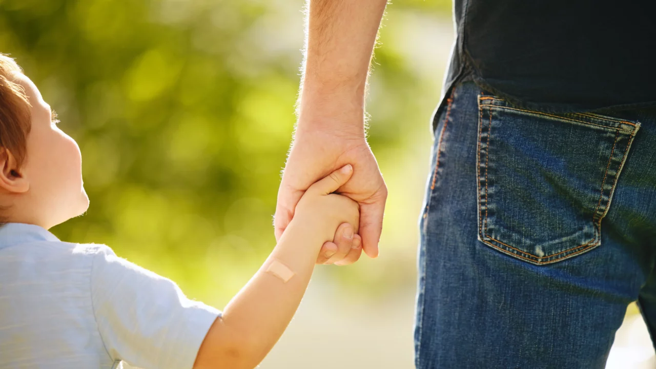 En dreng holder sin far i hånden, mens de går en tur