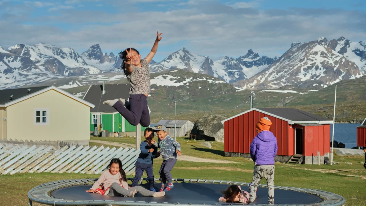 Nogle børn hopper på en trampolin med snedækkede bjerge i baggrunden