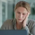Kvinde kigger træt på sin computerskærm i halvmørke omgivelser