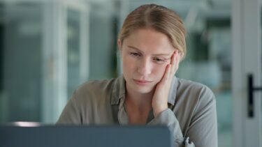 Kvinde kigger træt på sin computerskærm i halvmørke omgivelser