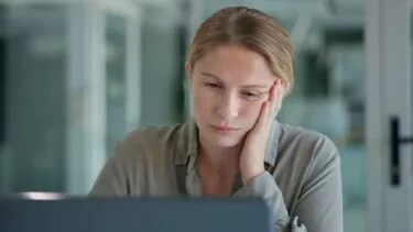 Kvinde kigger træt på sin computerskærm i halvmørke omgivelser