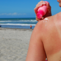 Kvinde på stranden - hun skal til at smøre solcreme på skulderen