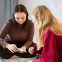 To unge piger sidder på en seng og kigger på en smartphone