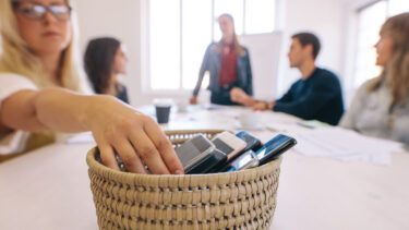 Folk på arbejde holder møde og lægger mobilerne væk i en kurv