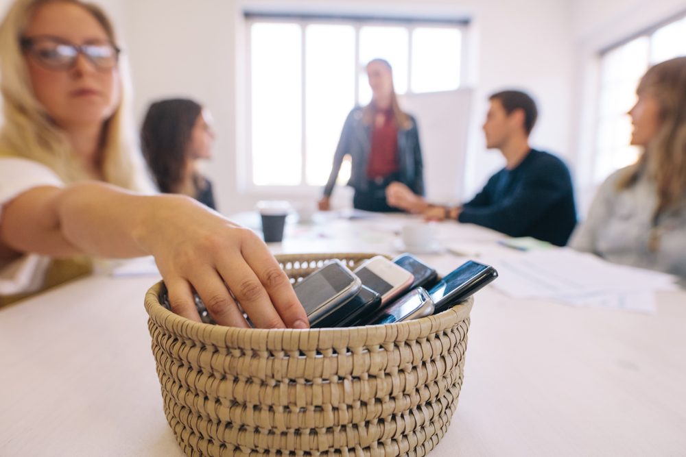 Folk på arbejde holder møde og lægger mobilerne væk i en kurv