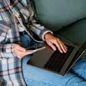 Kvinde i sofa med laptop på skødet tjekker mobilen