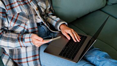 Kvinde i sofa med laptop på skødet tjekker mobilen