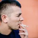 closeup af ung mand, der står op ad en mur og ryger en cigaret