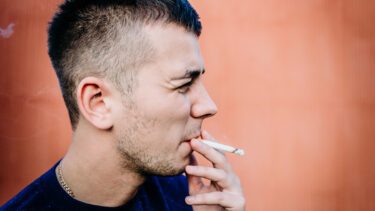 closeup af ung mand, der står op ad en mur og ryger en cigaret