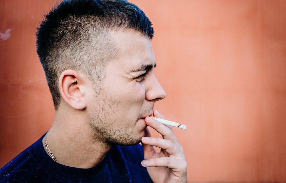 closeup af ung mand, der står op ad en mur og ryger en cigaret