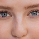 Nærbillede af en persons ansigt med fokus på de blå øjne, de lange øjenvipper og den lyse hud med fregner. Billedet viser detaljer af øjnene, øjenbrynene og den øverste del af næsen.