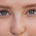 Nærbillede af en persons ansigt med fokus på de blå øjne, de lange øjenvipper og den lyse hud med fregner. Billedet viser detaljer af øjnene, øjenbrynene og den øverste del af næsen.