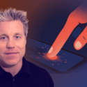 En mand med lyst hår og et lille smil er i forgrunden. I baggrunden rører en illustreret hånd ved skærmen på en digital enhed, hvilket skaber en glødende effekt. Billedet har en blå og orange gradient.