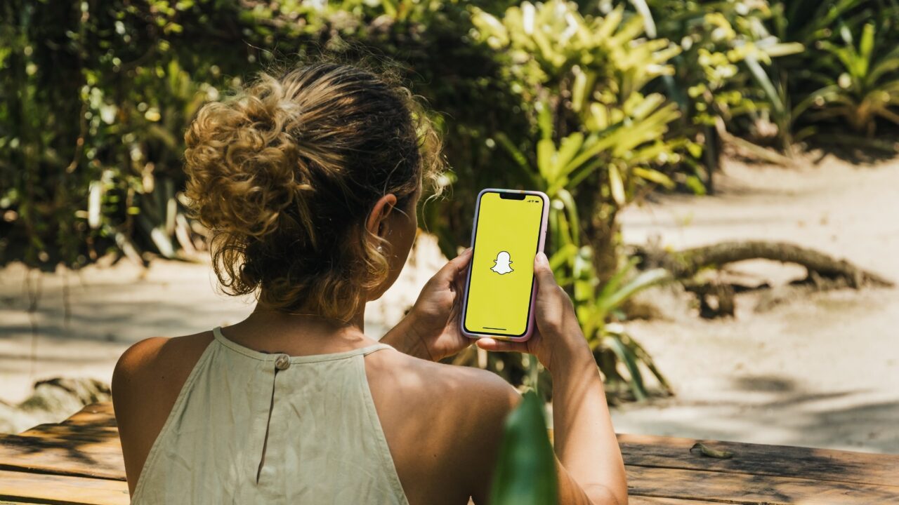 Ung pige holder en mobiltelefon i hånden. På skærmen er Snapchat-logoet.