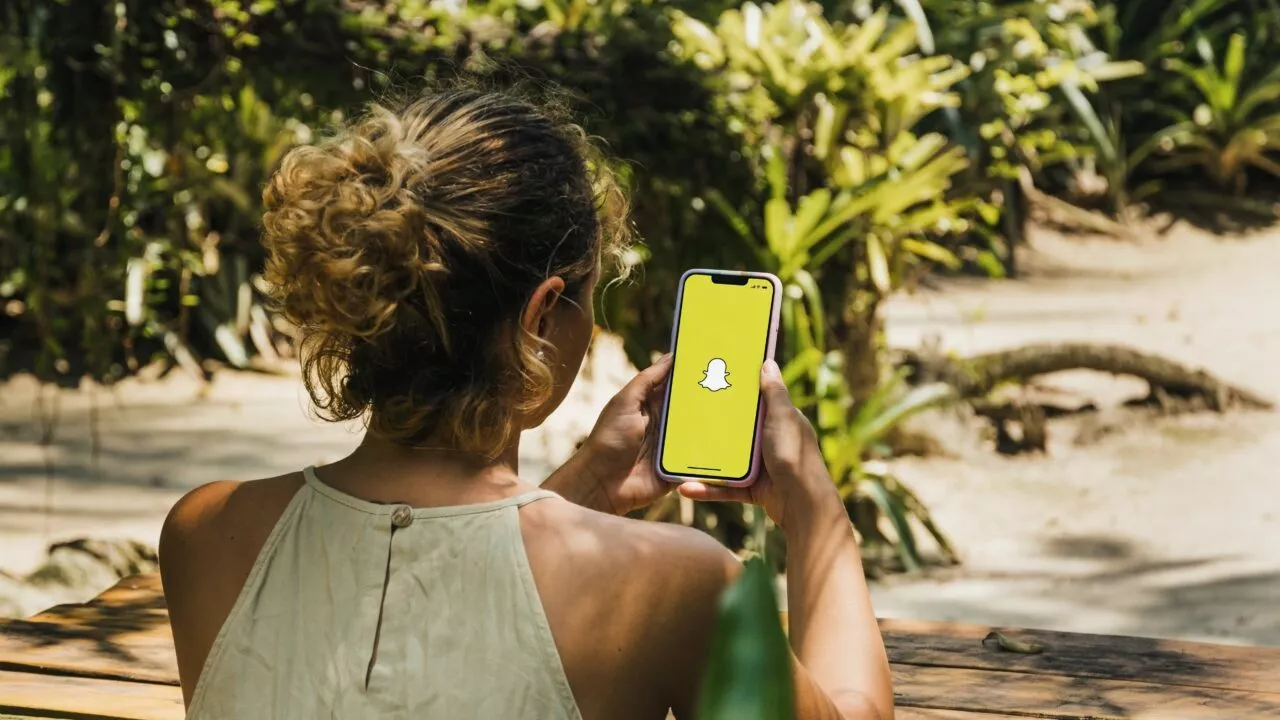 Ung pige holder en mobiltelefon i hånden. På skærmen er Snapchat-logoet.