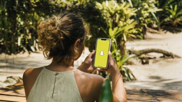 Ung pige holder en mobiltelefon i hånden. På skærmen er Snapchat-logoet.