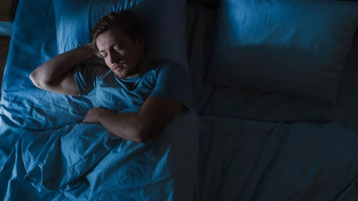 En mand ligger og sover i sin seng om natten, dækket af et blåt tæppe