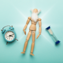 Trædukke med hvidt skæg ligger ved siden af et ur og et timeglas