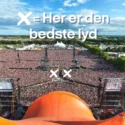 En stor udendørs musikfestival med en massiv menneskemængde foran en scene. Over billedet står en dansk tekst: X = Her er den bedste lyd med hvide X'er, der markerer midten og fronten af publikum for den bedste lyd.