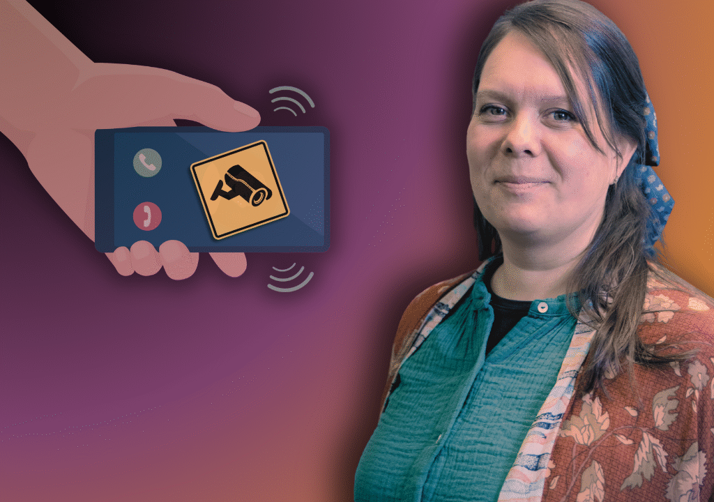 Tanja Kammersgaard Christensen står foran en illustration af en hånd, der holder en smartphone med et overvågningskameraikon på skærmen, på en lilla og orange baggrund.