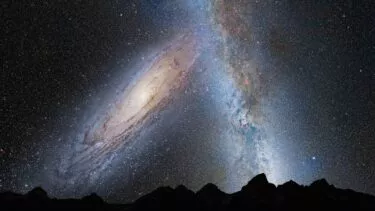 En fantastisk nattehimmel viser Mælkevejen og Andromeda-galaksen over en silhuet af forrevne bjergtoppe, fyldt med utallige stjerner og kosmiske skyer.