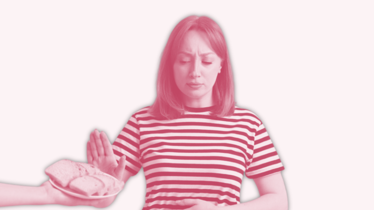 En kvinde i stribet skjorte holder sig for maven med den ene hånd og løfter den anden hånd for at afvise en tallerken brød, der bliver tilbudt hende. Billedet har en pink nuance og en almindelig baggrund.