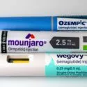 Tre fyldte injektionspenne mærket Ozempic, Mounjaro og Wegovy, der alle bruges til at behandle diabetes eller fedme, er placeret side om side på en hvid overflade.