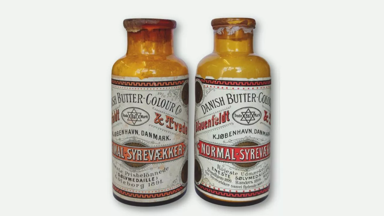 To vintage gule glasflasker mærket Danish Butter Colour med sort, rød og hvid tekst, der viser et stjernesymbol og dansk skrift. Begge flasker har slidte etiketter og brune kapsler.