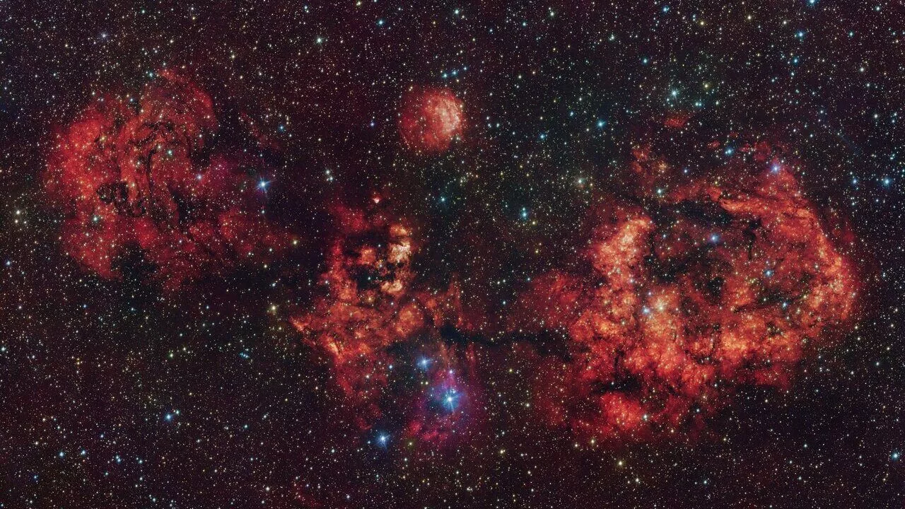 En stjernefyldt nattehimmel viser levende røde tåger og skyer af kosmisk støv, oplyst af utallige klare stjerner spredt ud over det ydre rums mørke vidder.