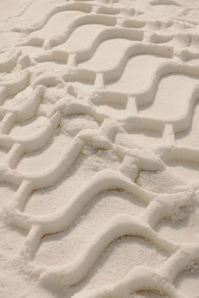 Bølgede dækmønstre er præget i glat, lyst sand og skaber et gentagende geometrisk design på tværs af overfladen.