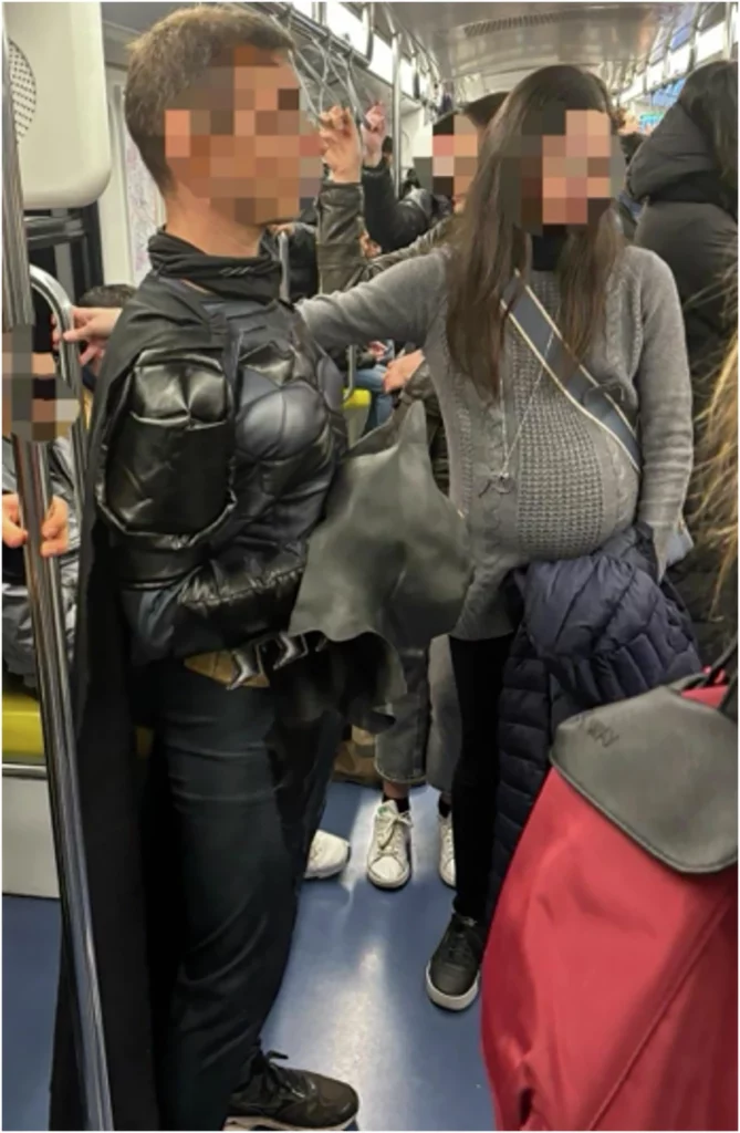 En person i Batman-kostume står i et overfyldt metrotog blandt andre passagerer. Ansigter er pixeleret af hensyn til privatlivets fred.