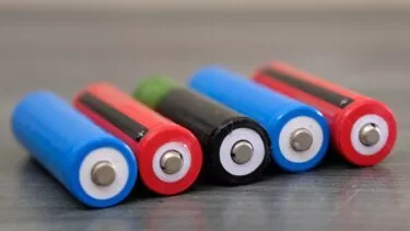 Nærbillede af fem AA-batterier, der ligger på siden i en række, med blå, røde, grønne og sorte hylstre synlige, alle med deres positive terminaler vendt fremad.