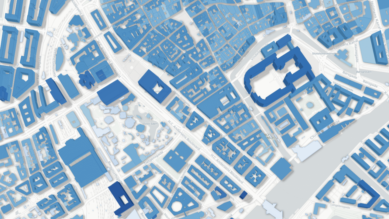 Et digitalt kort viser et byområde med gader og bygninger i forskellige blå nuancer, der fremhæver forskellige blok- og bygningsformer i en overhead-visning i 3D-stil. Ingen etiketter eller gadenavne er synlige.