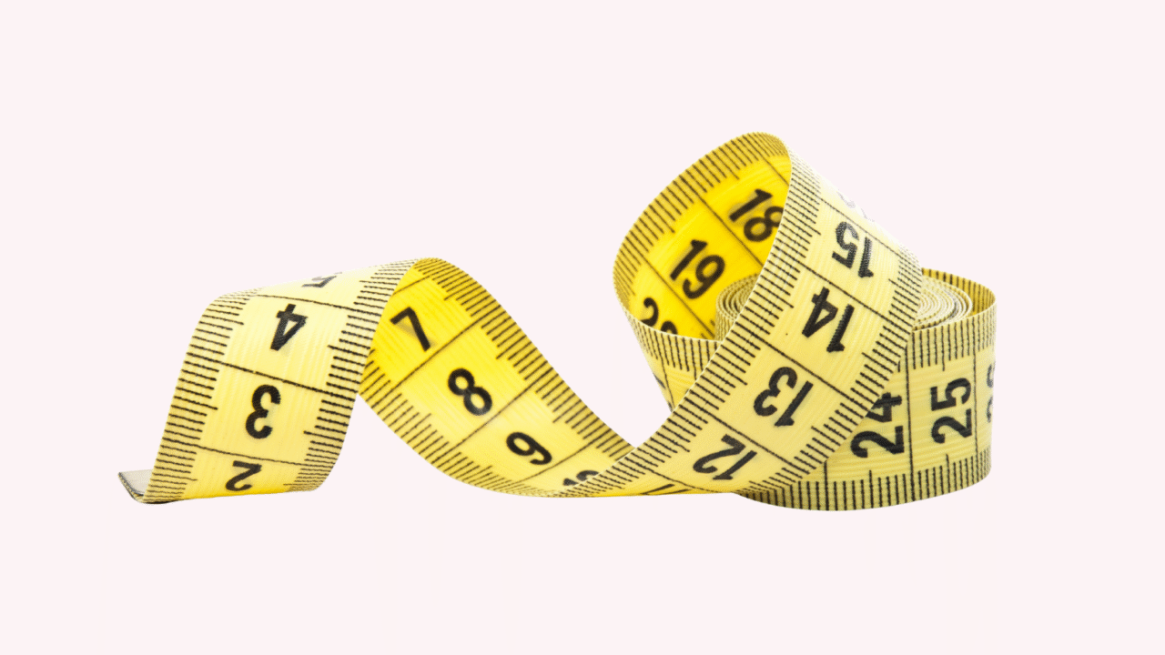 Et gult målebånd med sorte tal er løst oprullet på en lys, ensfarvet baggrund.