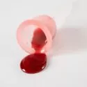 En lyserød menstruationskop, der er væltet på en hvid overflade, med mørkerød væske, der løber ud af den.