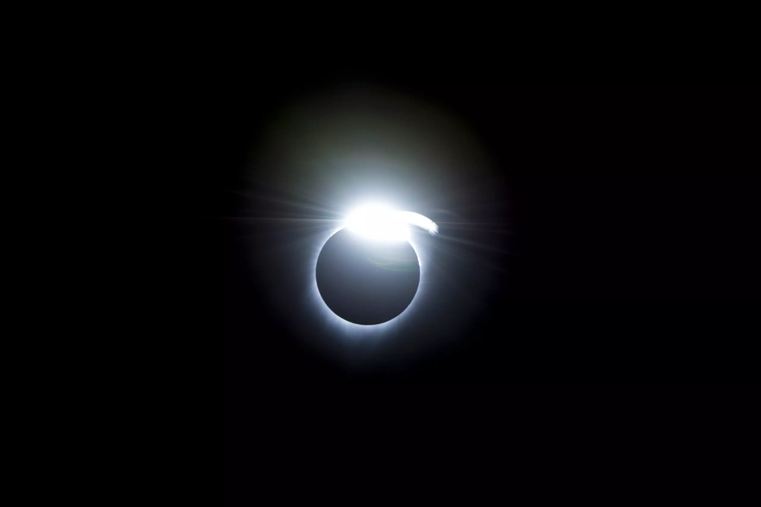 En solformørkelse, hvor solens lysende korona stråler omkring månens mørke silhuet og skaber en glødende ring på den sorte himmel.
