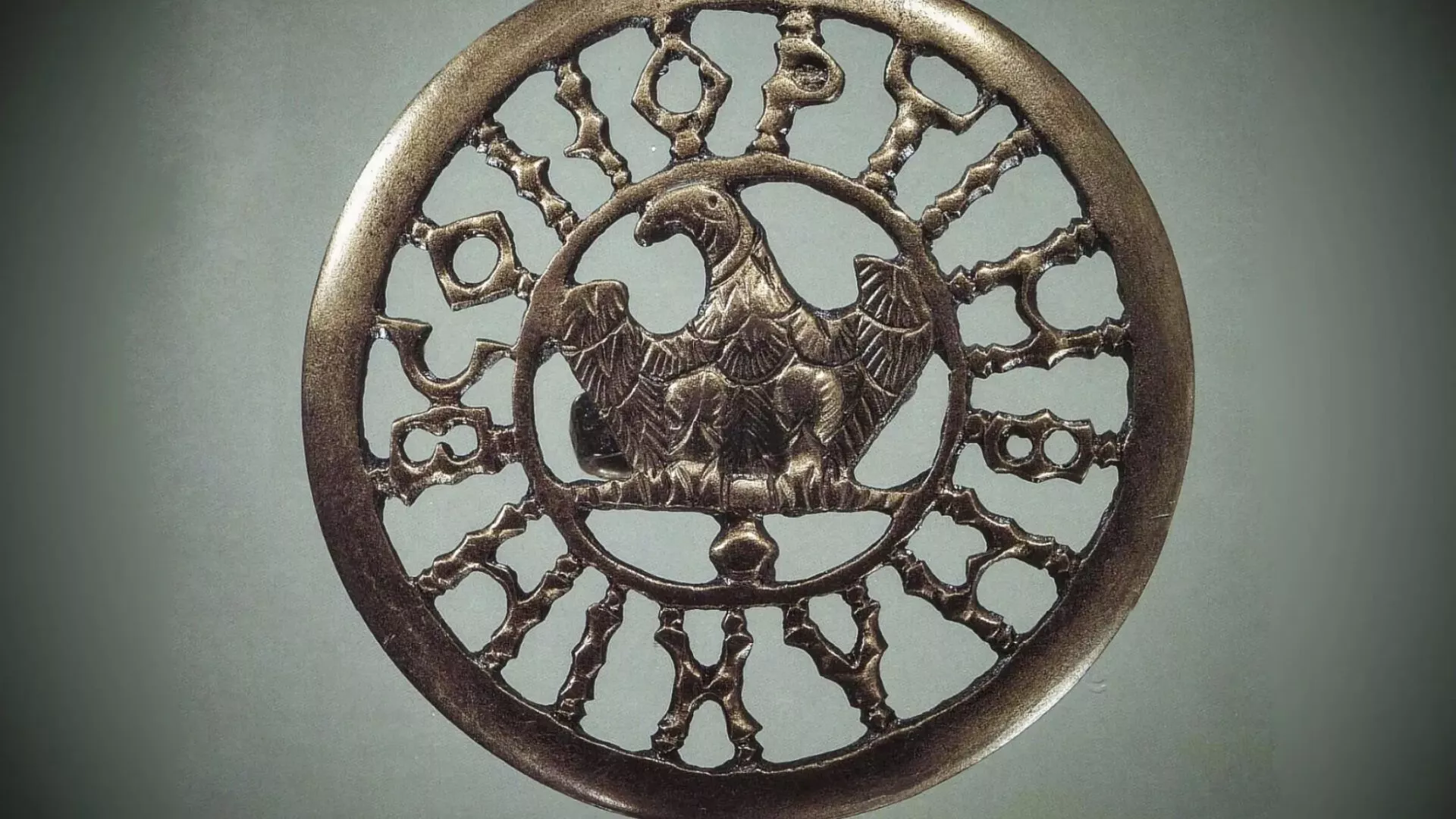 En rund bronzemedaljon med en ørn i midten med udstrakte vinger. Det gennembrudte design har dekorative mønstre og romertal som en urskive-her ses et bandolérbeslag som tilhørte én af soldaterne i hæren.